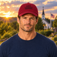 Male model wearing the cranberry Faith Courage Freedom hat in the matching sunset setting